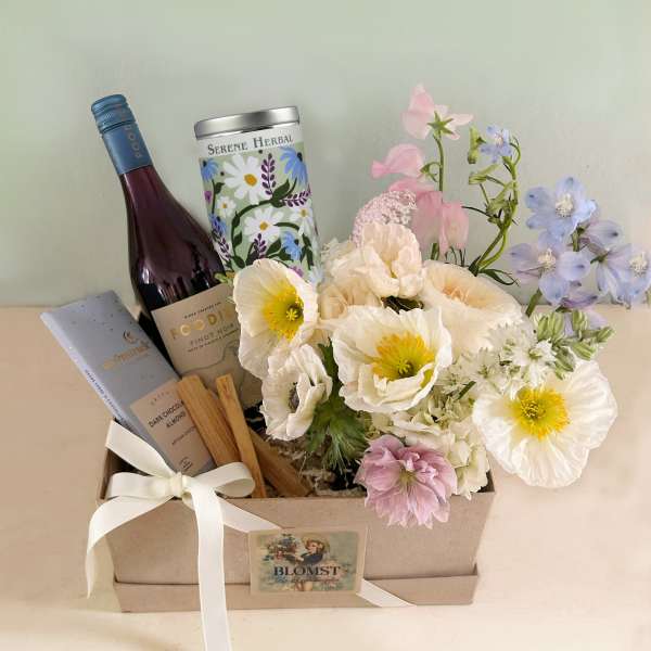 Gift box with flowers, wine, and chocolate bar tied with a white ribbon
