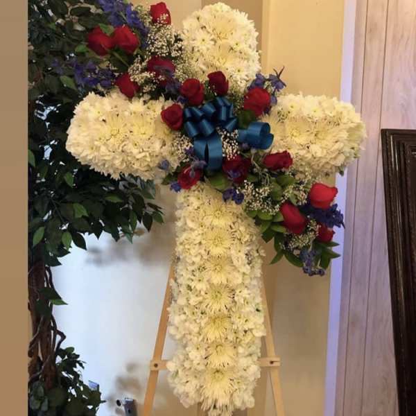 Cross-shaped floral tribute with white flowers, red roses, and a blue ribbon