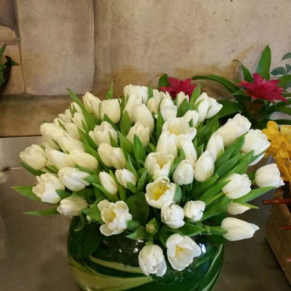 White tulips arranged in a round green glass vase