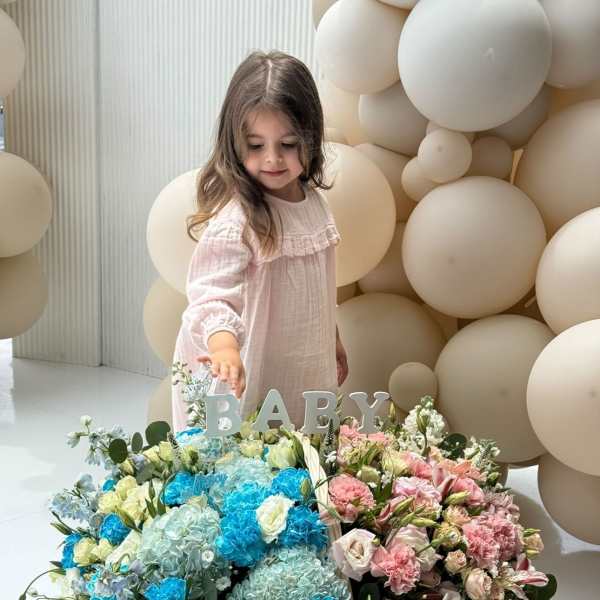 Large pastel flower basket with a BABY sign and a child standing behind it