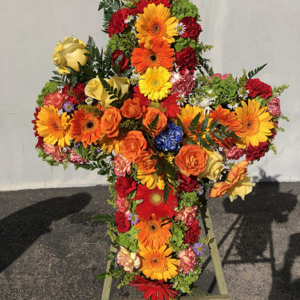 Cross-shaped floral spray with bright mixed blooms on a stand