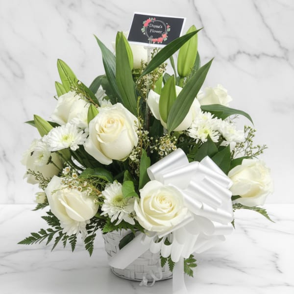 White roses and lilies arranged in a basket with a white ribbon