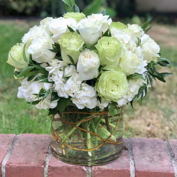 White and pale green roses arranged in a clear glass vase