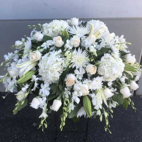 White floral casket spray with roses, lilies, and hydrangeas