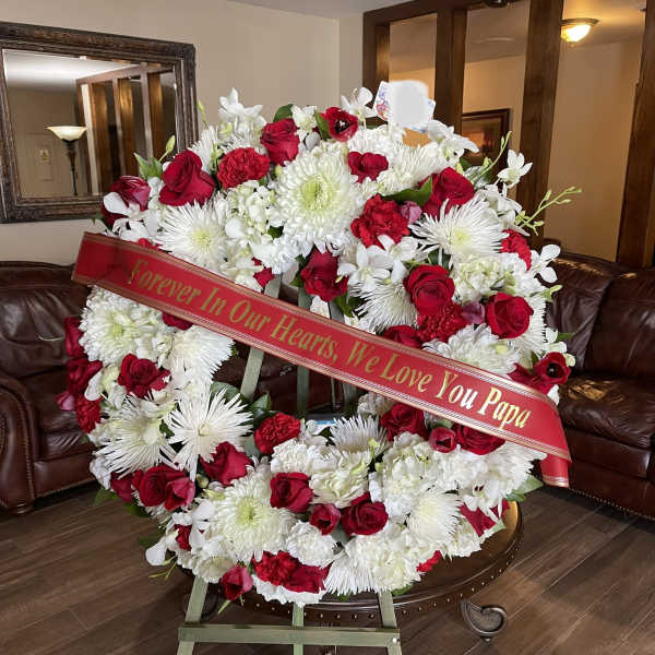 Large red and white funeral wreath on an easel with a memorial ribbon