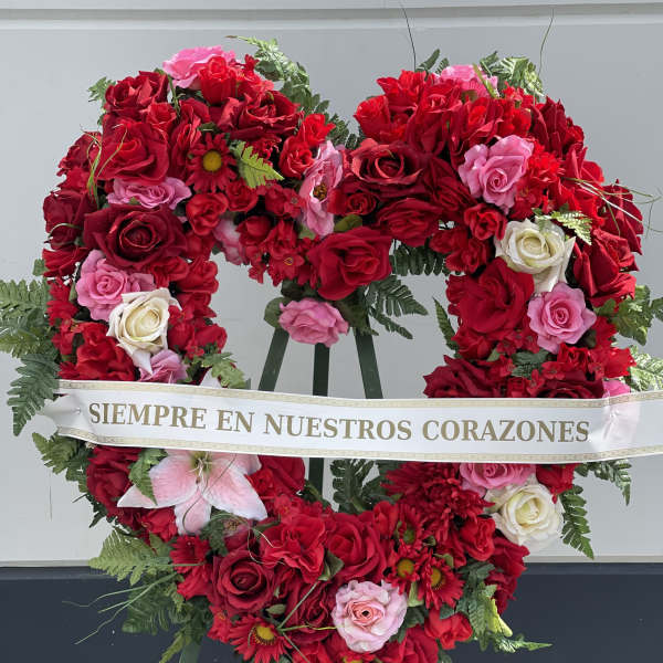 Heart-shaped floral wreath of red and pink roses with a memorial ribbon