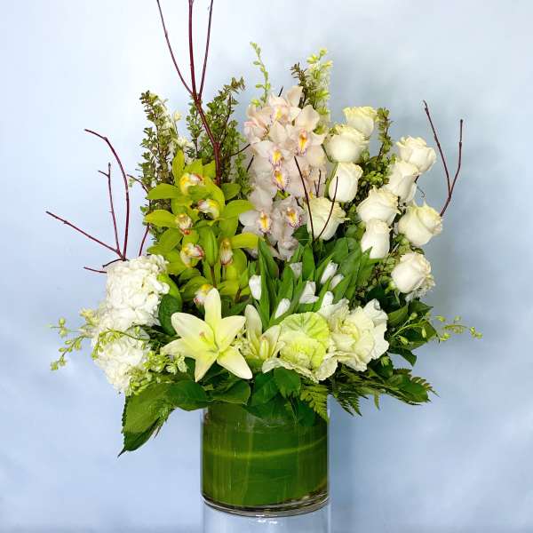 White roses, orchids, and lilies arranged in a green glass vase