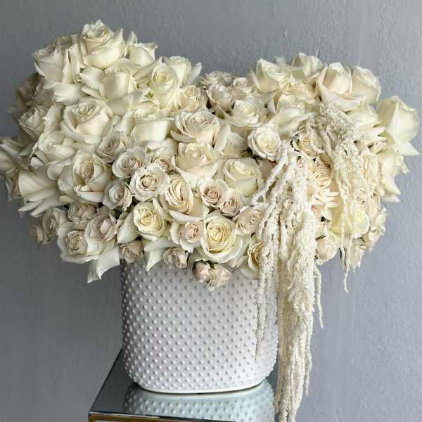White rose arrangement in a textured white vase with trailing white accents