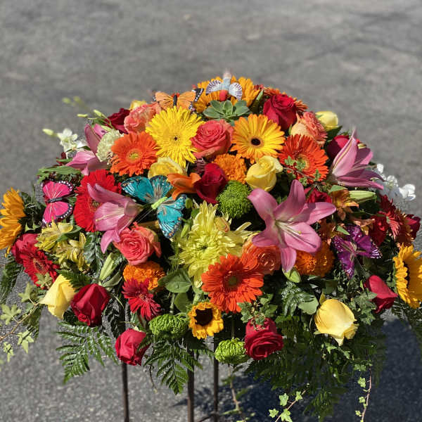 Colorful mixed flower arrangement on a stand with roses, gerbera daisies, lilies, and butterflies
