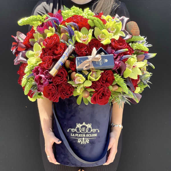 Large bouquet of red roses and lime-green orchids in a navy hatbox with chocolates