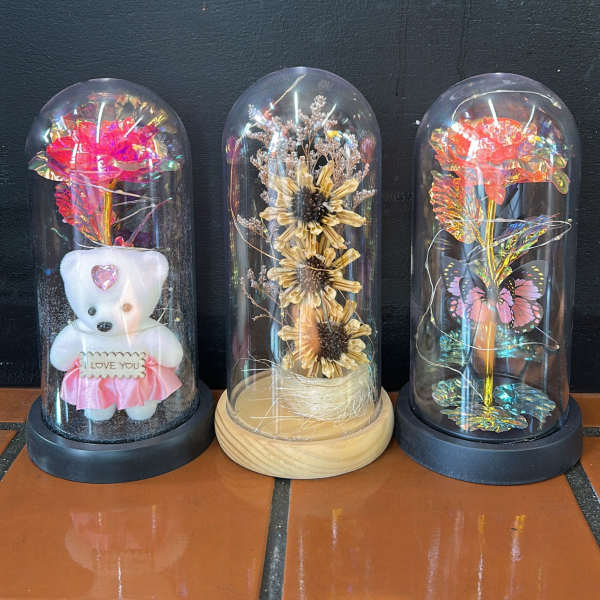 Three decorative dome displays with preserved flowers and a teddy bear.