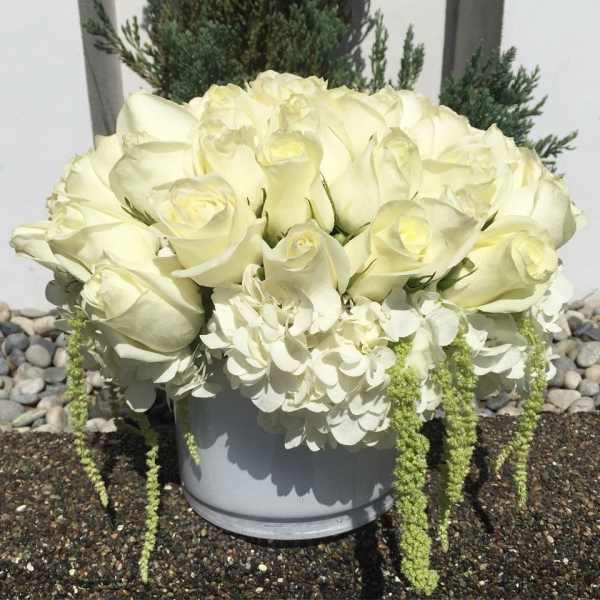 White rose arrangement in a gray container with trailing white blooms