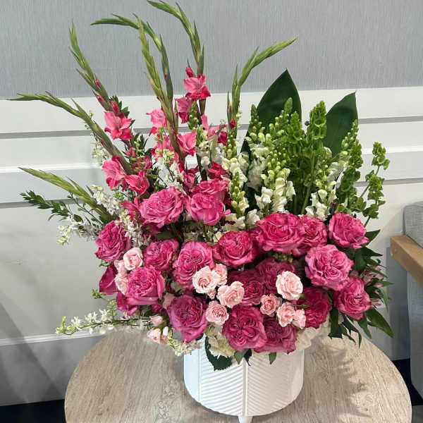 Large pink and white floral arrangement with roses and snapdragons in a white ceramic pot.