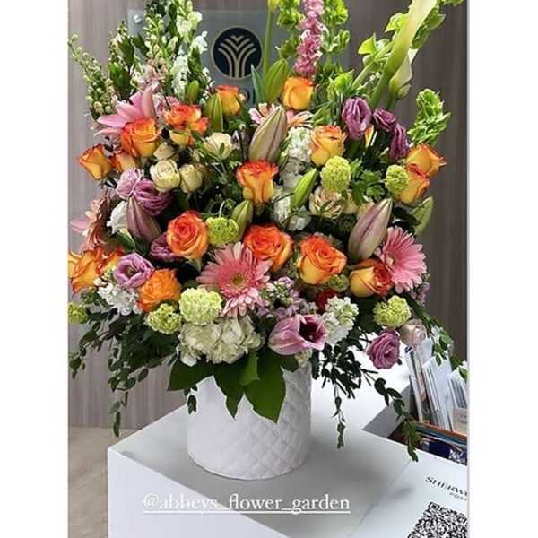 Tall mixed bouquet in a white textured vase with orange, pink, and purple flowers