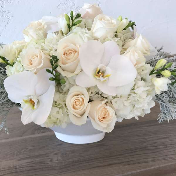 White roses and orchids in a low white bowl