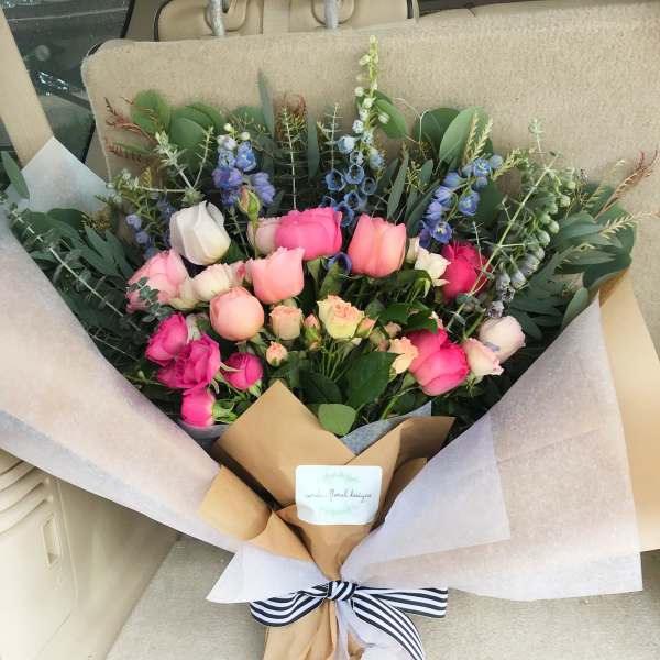 Bouquet of pink and blue flowers wrapped in paper with a striped ribbon