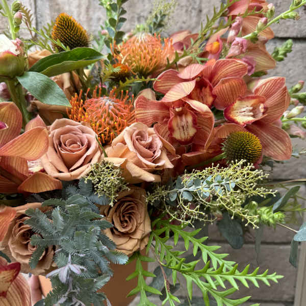 Peach roses and orange orchids in a terracotta vase