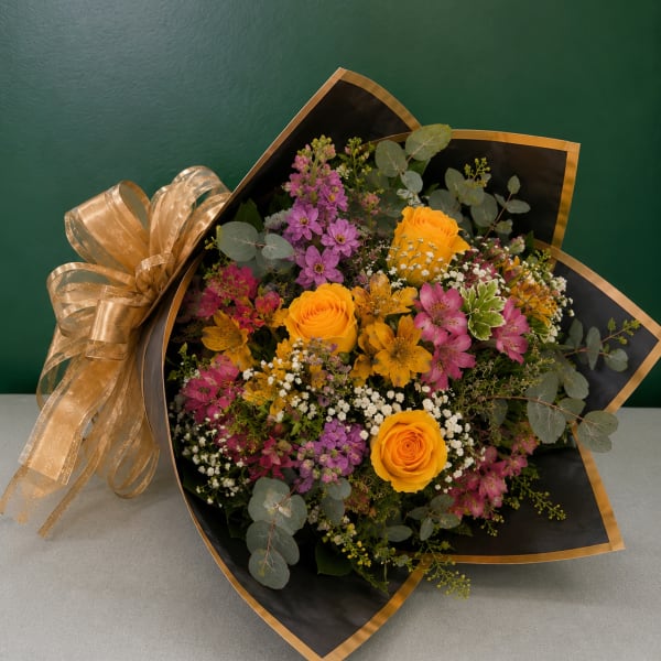 Bouquet of yellow roses and pink-purple mixed flowers wrapped in black paper with gold trim