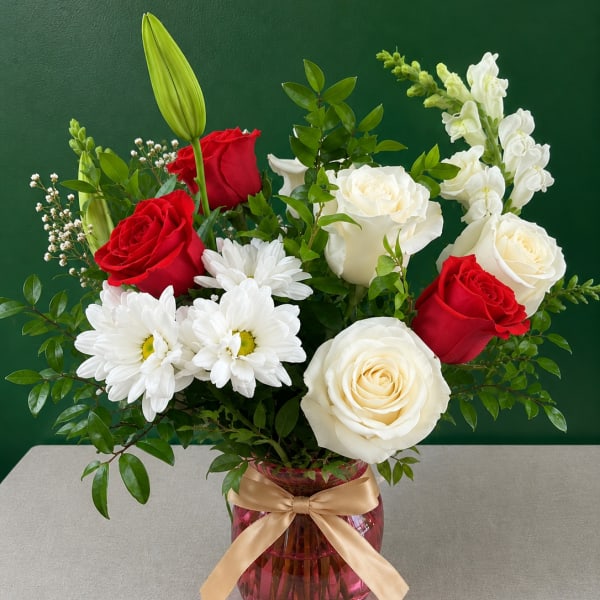 Red and white roses with daisies in a pink vase with a gold ribbon