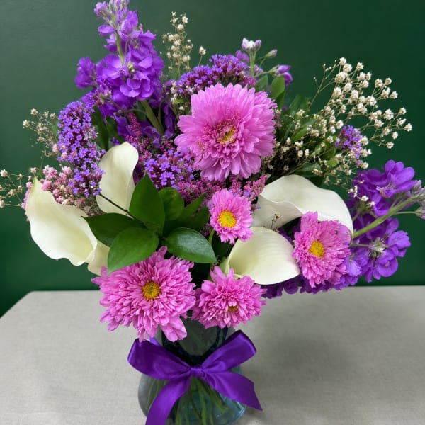 Purple and pink mixed bouquet with white calla lilies in a glass vase