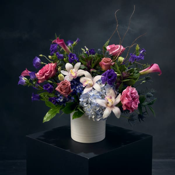 Mixed bouquet of pink, purple, and white flowers in a white vase