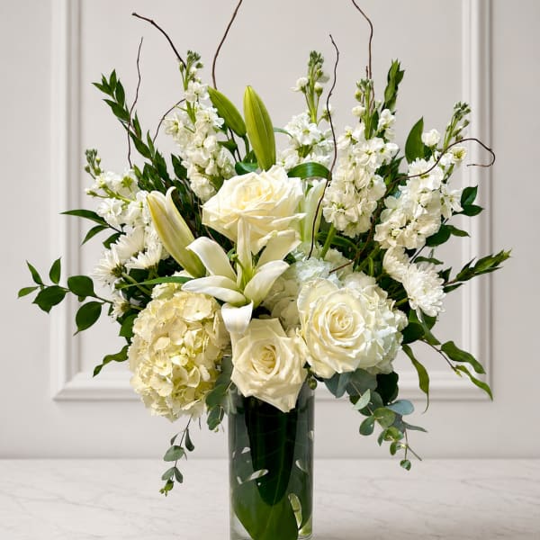 White roses and lilies arranged in a tall glass vase