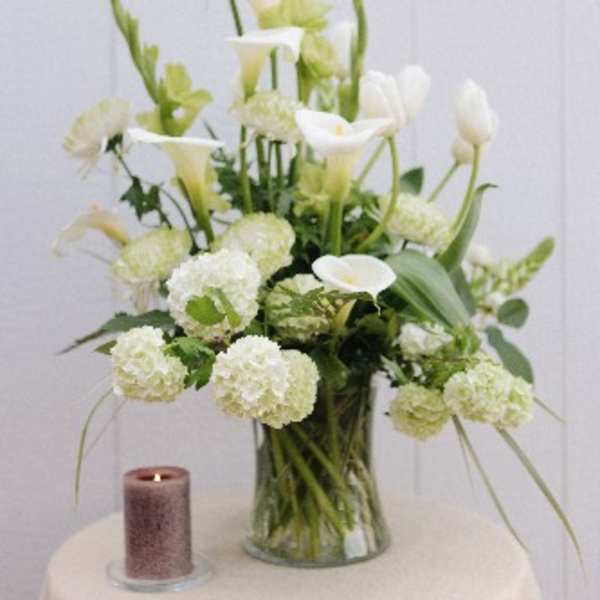 White calla lilies and round white blooms in a glass vase