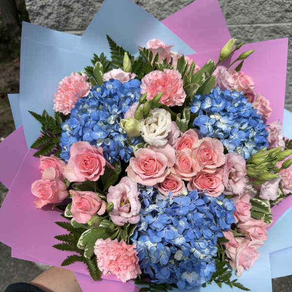 Bouquet of blue hydrangeas, pink roses, and carnations wrapped in pastel paper