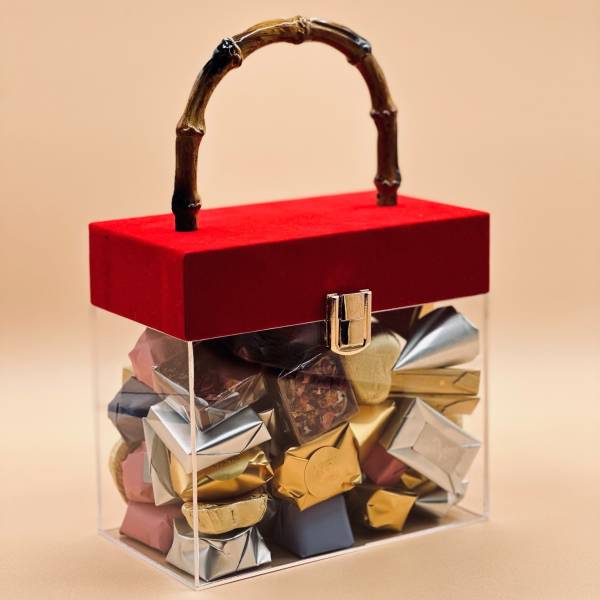 Clear gift box with a red lid and assorted wrapped chocolates inside