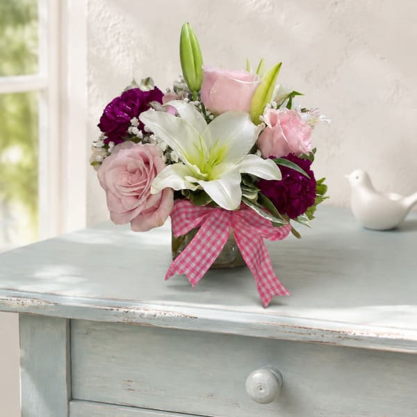 Pink and white flower arrangement in a glass vase with a gingham ribbon