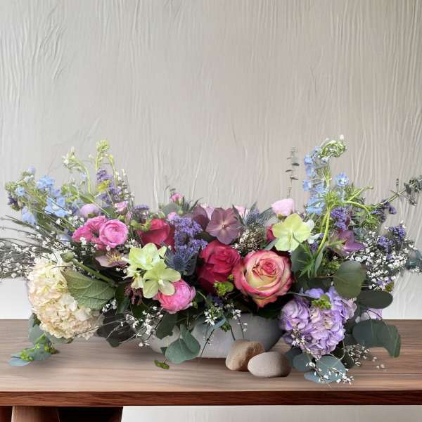 Low floral centerpiece with pink, purple, and blue blooms in a gray container