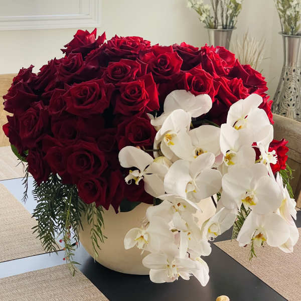 Large arrangement of red roses with white orchids in a cream vase