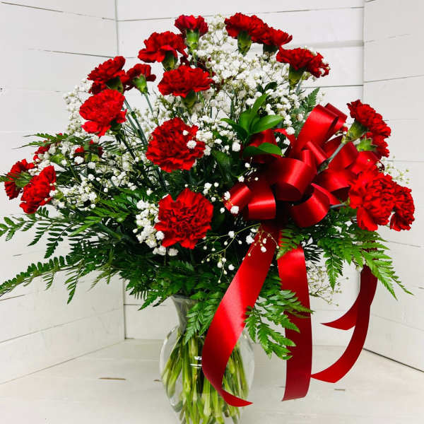 Red carnations and white baby's breath in a clear glass vase with a red ribbon