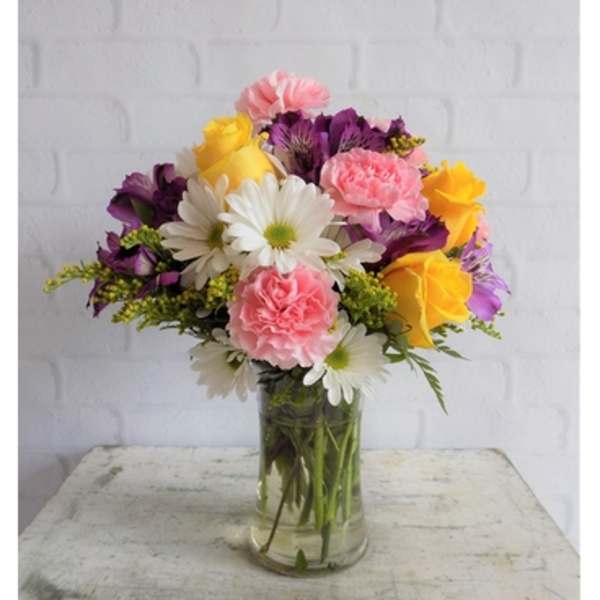 Yellow roses, pink carnations, white daisies, and purple blooms in a clear glass vase