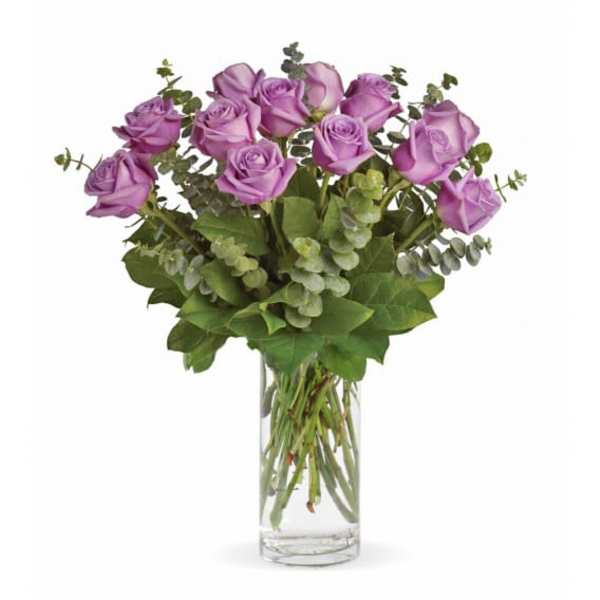 Purple roses in a clear glass vase with eucalyptus