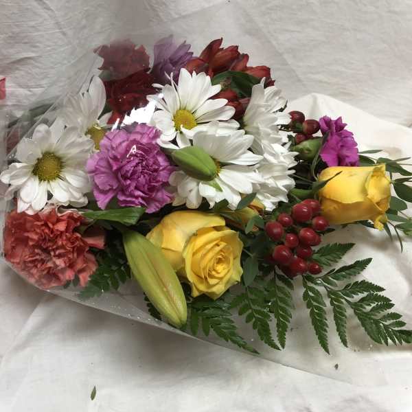 Mixed bouquet of daisies, roses, carnations, and lilies wrapped in clear plastic