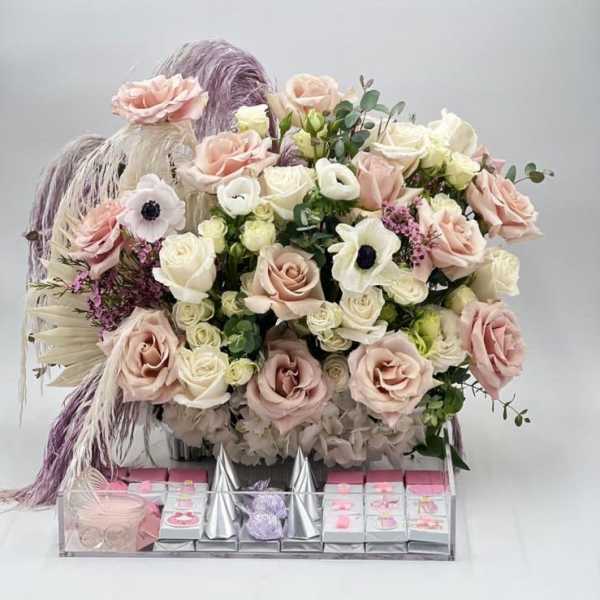 Large pastel rose arrangement with candles and gift boxes in a clear tray