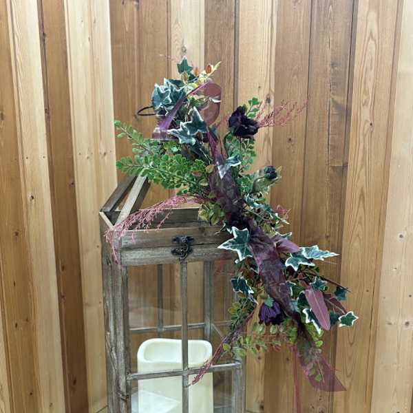 Decorative lantern with faux greenery and dark purple flowers