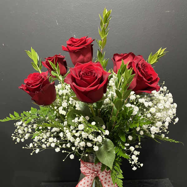 Red roses in a clear glass vase with baby's breath and a ribbon