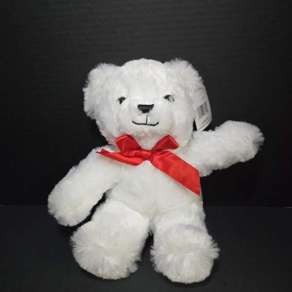 White teddy bear with a red ribbon bow on a black background