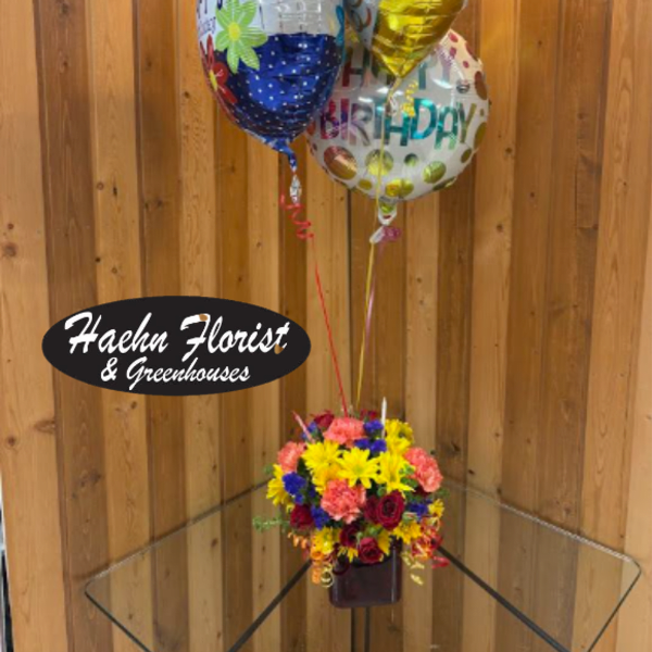 Birthday balloons above a colorful flower arrangement in a vase