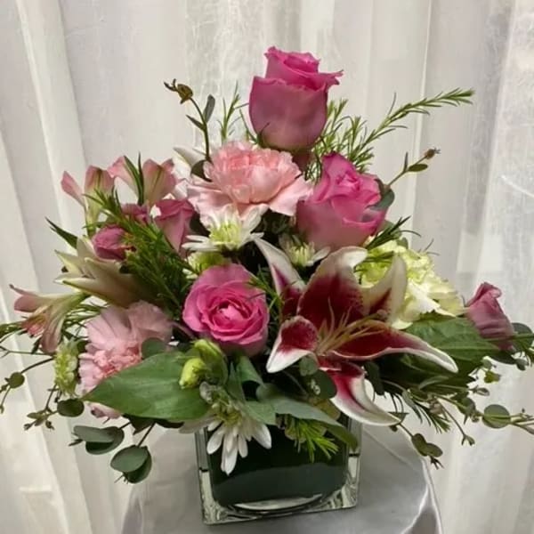 Pink roses and lilies arranged in a square glass vase