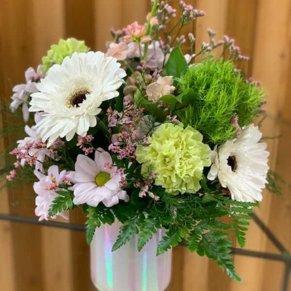 Pastel flower arrangement in a white vase with white daisies and green carnations