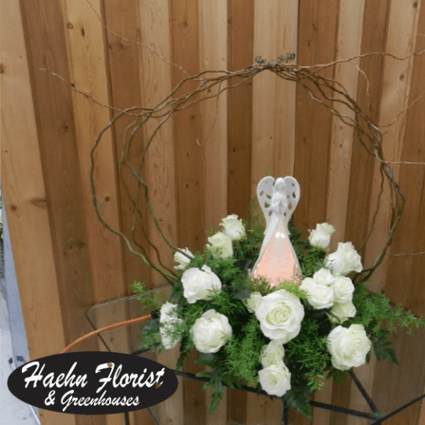 White roses arranged around a small angel figurine in a circular twig frame