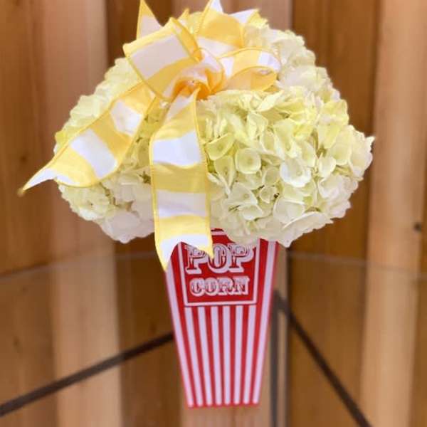 White hydrangea arrangement in a popcorn container with a yellow ribbon