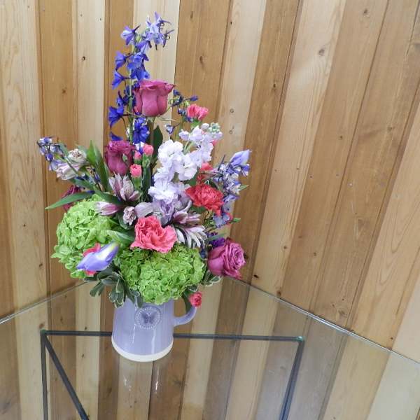 Mixed bouquet in a lavender pitcher vase with pink, purple, and green blooms