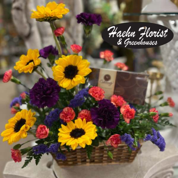 Basket arrangement with yellow sunflowers, purple carnations, and pink spray carnations