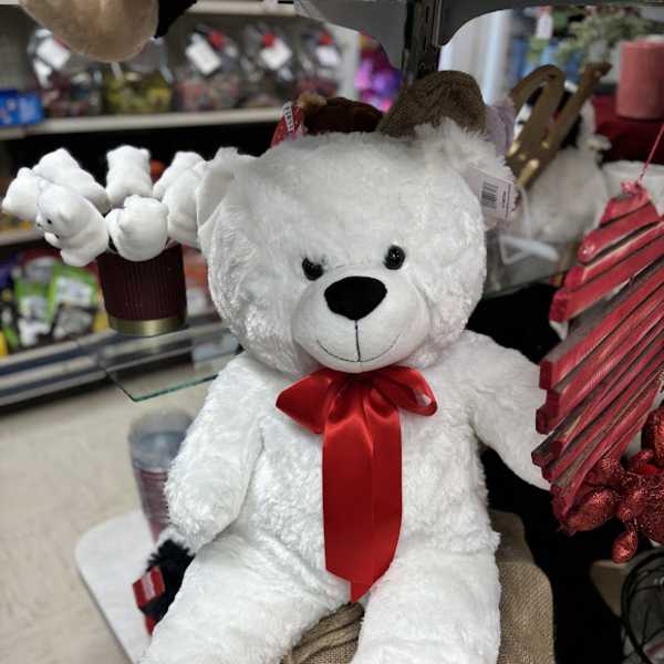 White teddy bear with a red ribbon sitting among gift items