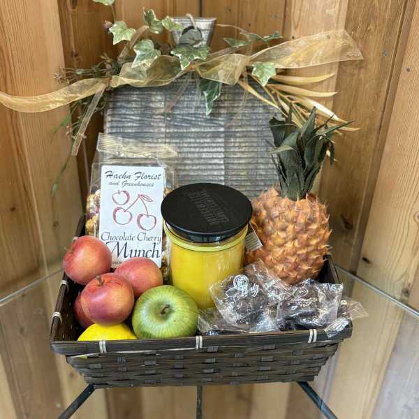 Fruit gift basket with pineapple, apples, peaches, candy, and a jar candle