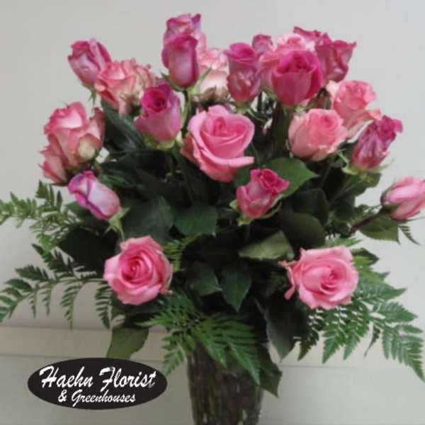 Pink roses arranged in a clear glass vase with fern accents.